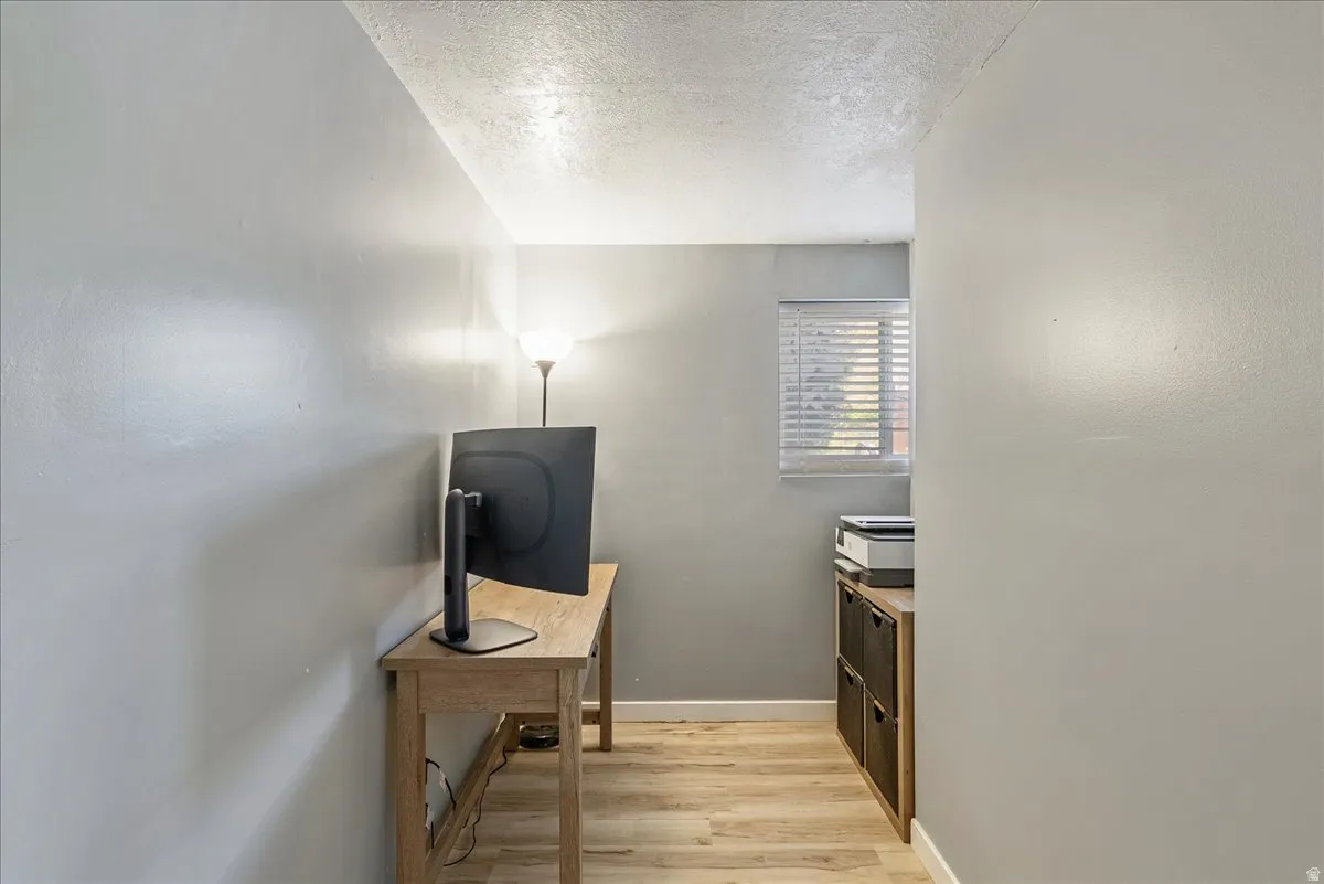 Hall with a textured ceiling, light wood finished floors, and an office area