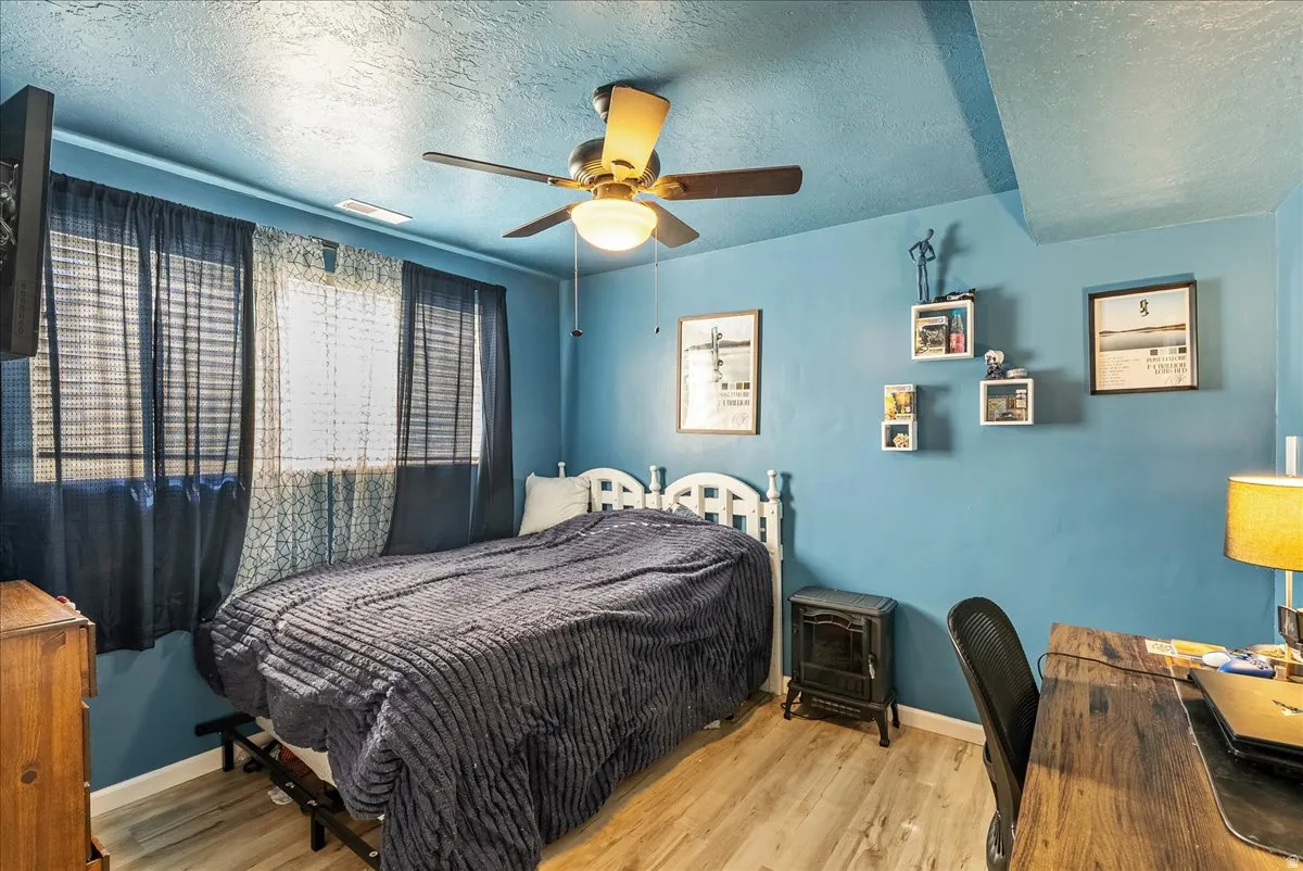 Bedroom featuring wood finished floors, a textured ceiling, a ceiling fan, and an office area