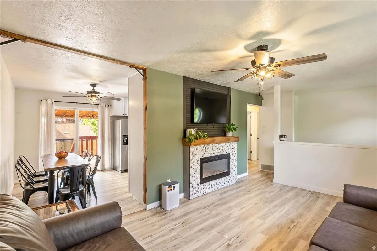 Living area featuring a ceiling fan, a textured ceiling, light wood-style flooring, and a fireplace