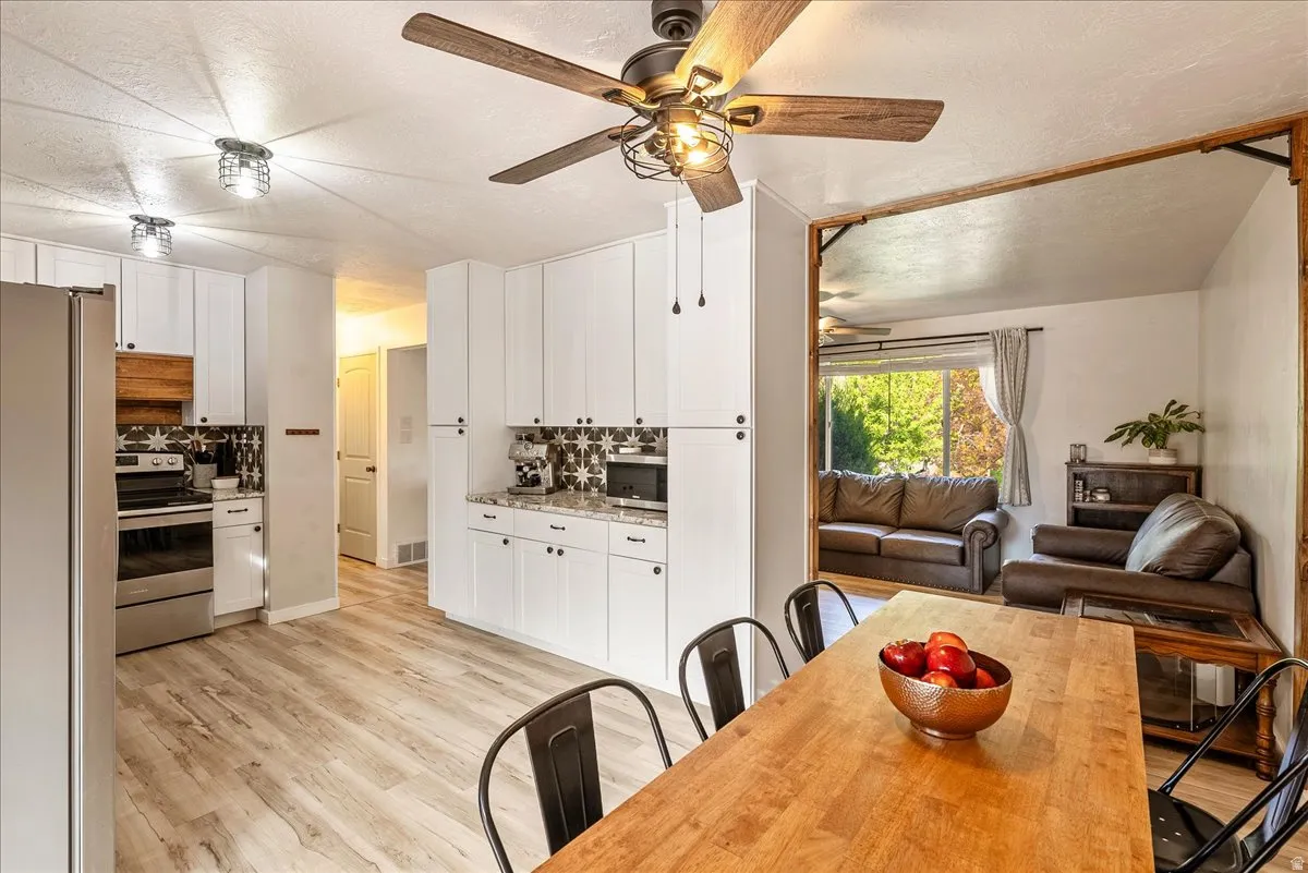 Kitchen with stainless steel appliances, a textured ceiling, white cabinets, light wood-style floors, and backsplash
