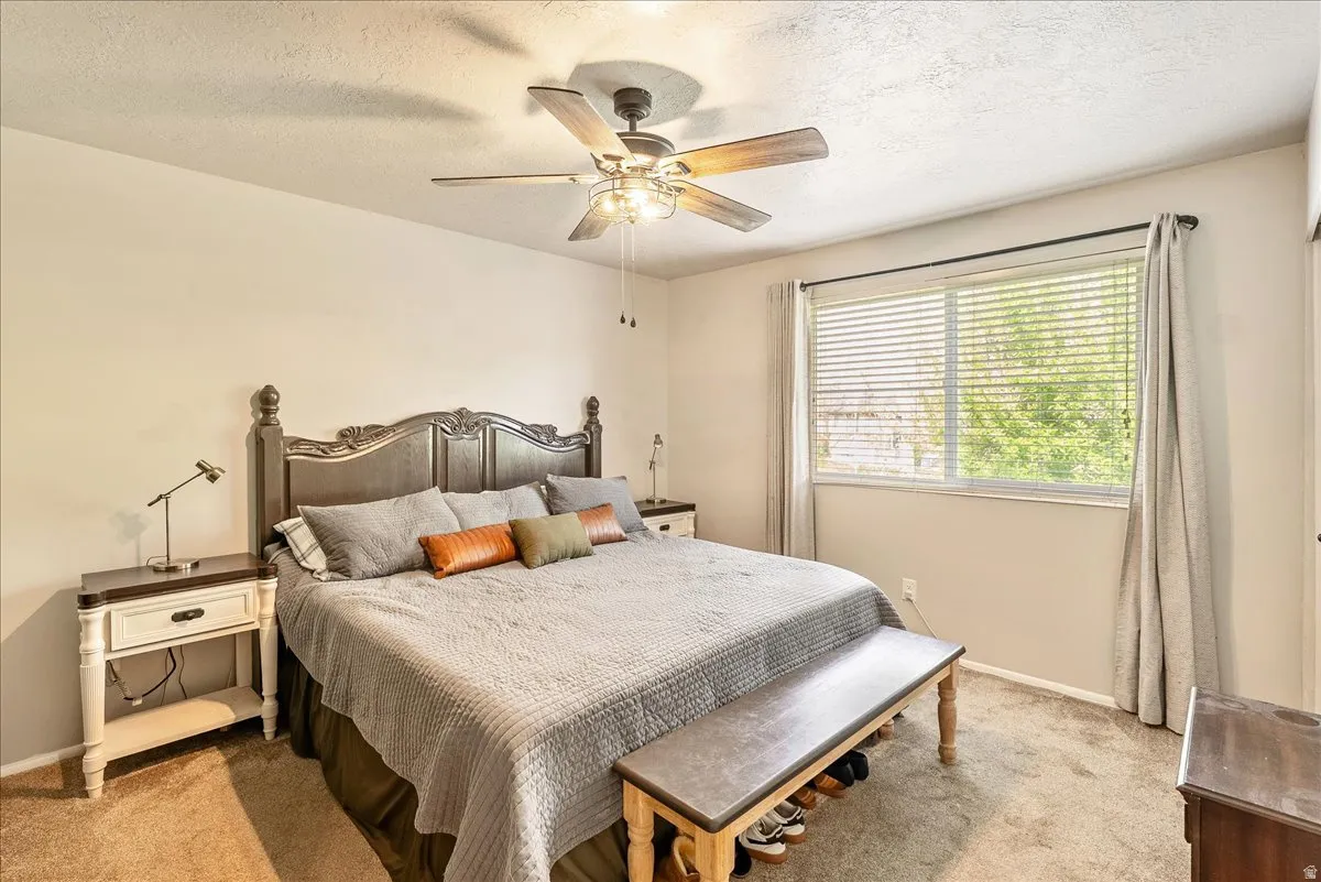 Bedroom with light colored carpet, a textured ceiling, and ceiling fan