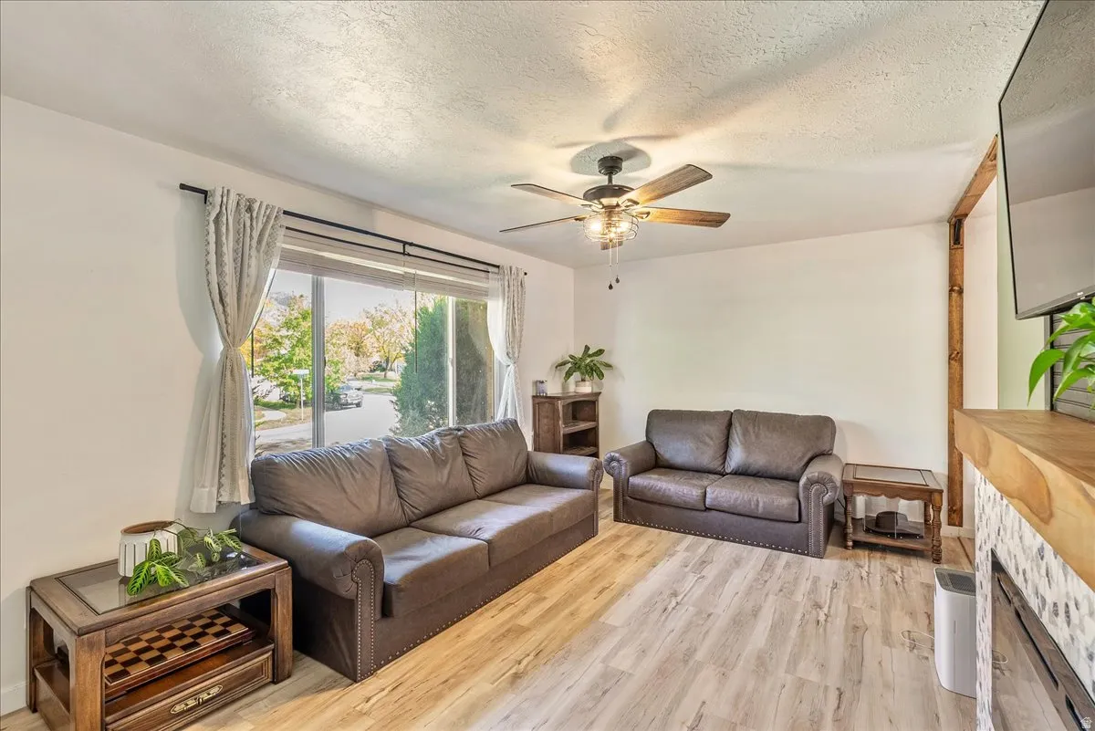 Living room with light wood-type flooring, a ceiling fan, and a textured ceiling