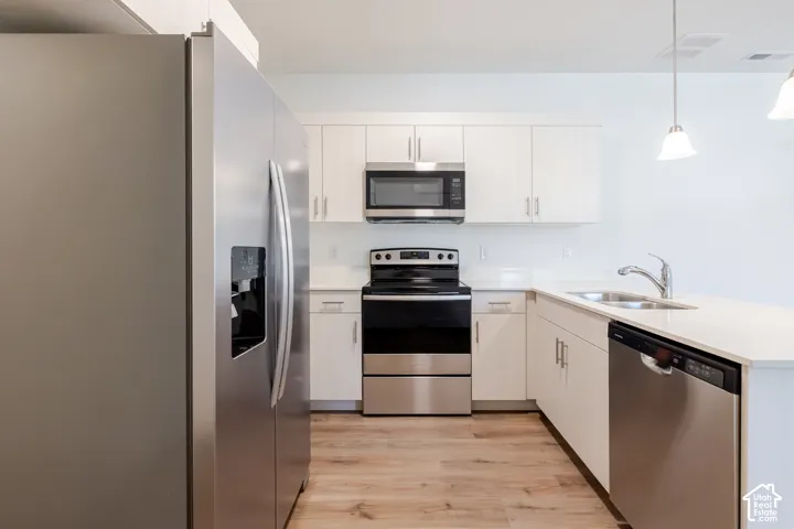 Kitchen featuring stainless steel appliances, white cabinetry, solid surface countertops, and wood-finish flooring