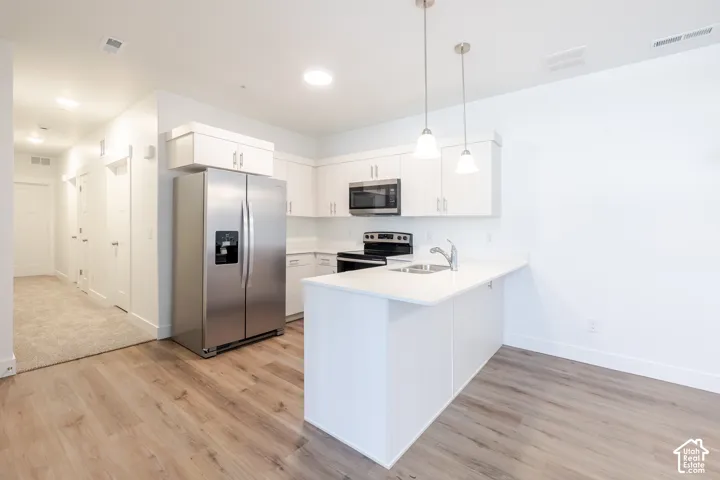 Kitchen featuring stainless steel appliances, white cabinetry, a kitchen island with a sink, and wood-finish flooring
