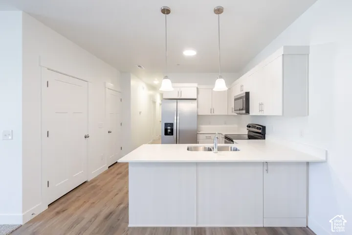Kitchen featuring a stainless steel refrigerator, black stove, microwave, white cabinetry, and a center island with an undermount sink
