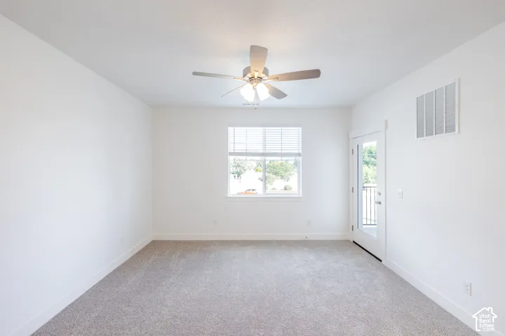 Carpeted room with a ceiling fan, window with blinds, and a glass-paneled door leading to an exterior balcony with black railings