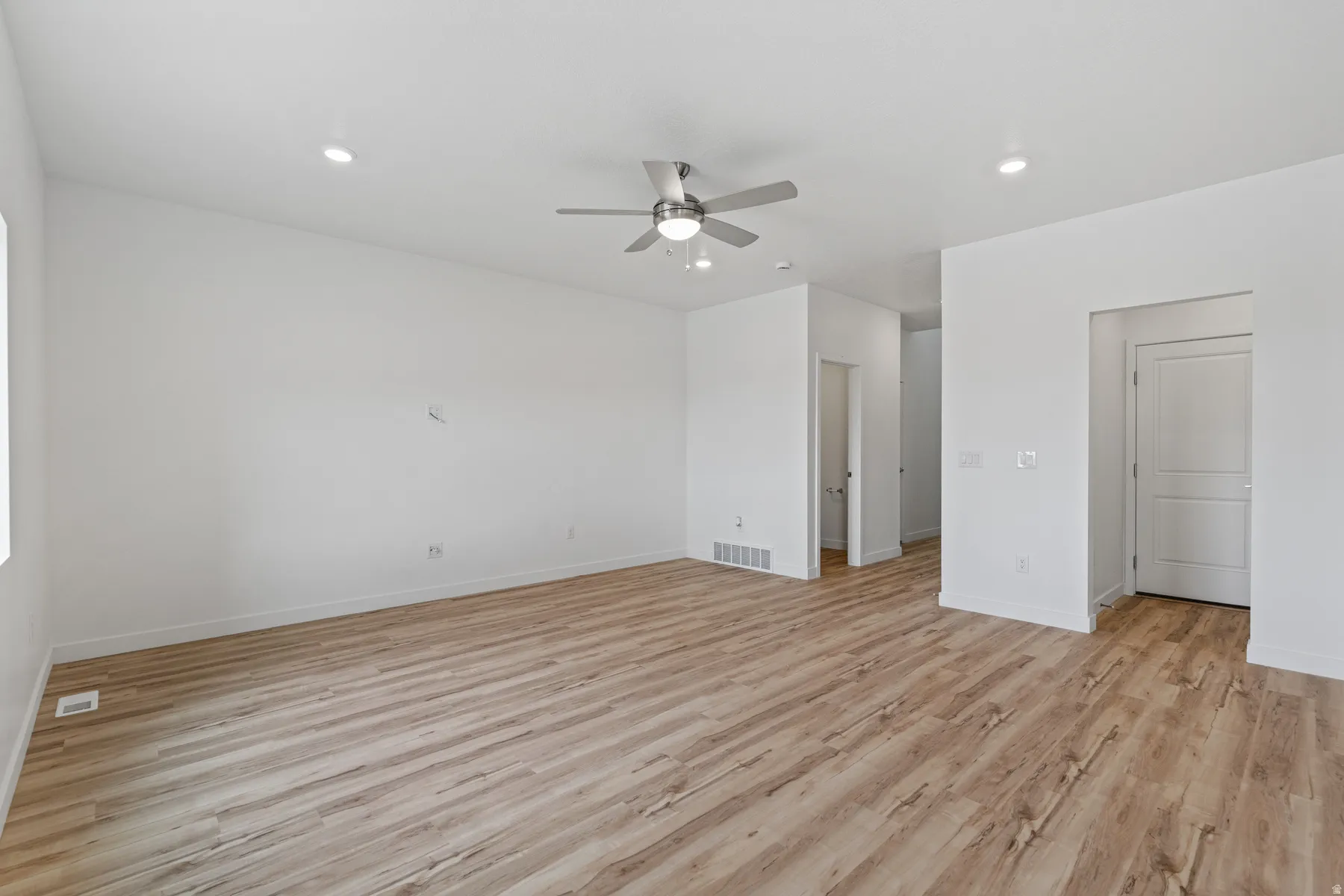 Spacious room featuring wood-finish flooring, recessed lighting, a ceiling fan with integrated light, white baseboards, and white painted walls