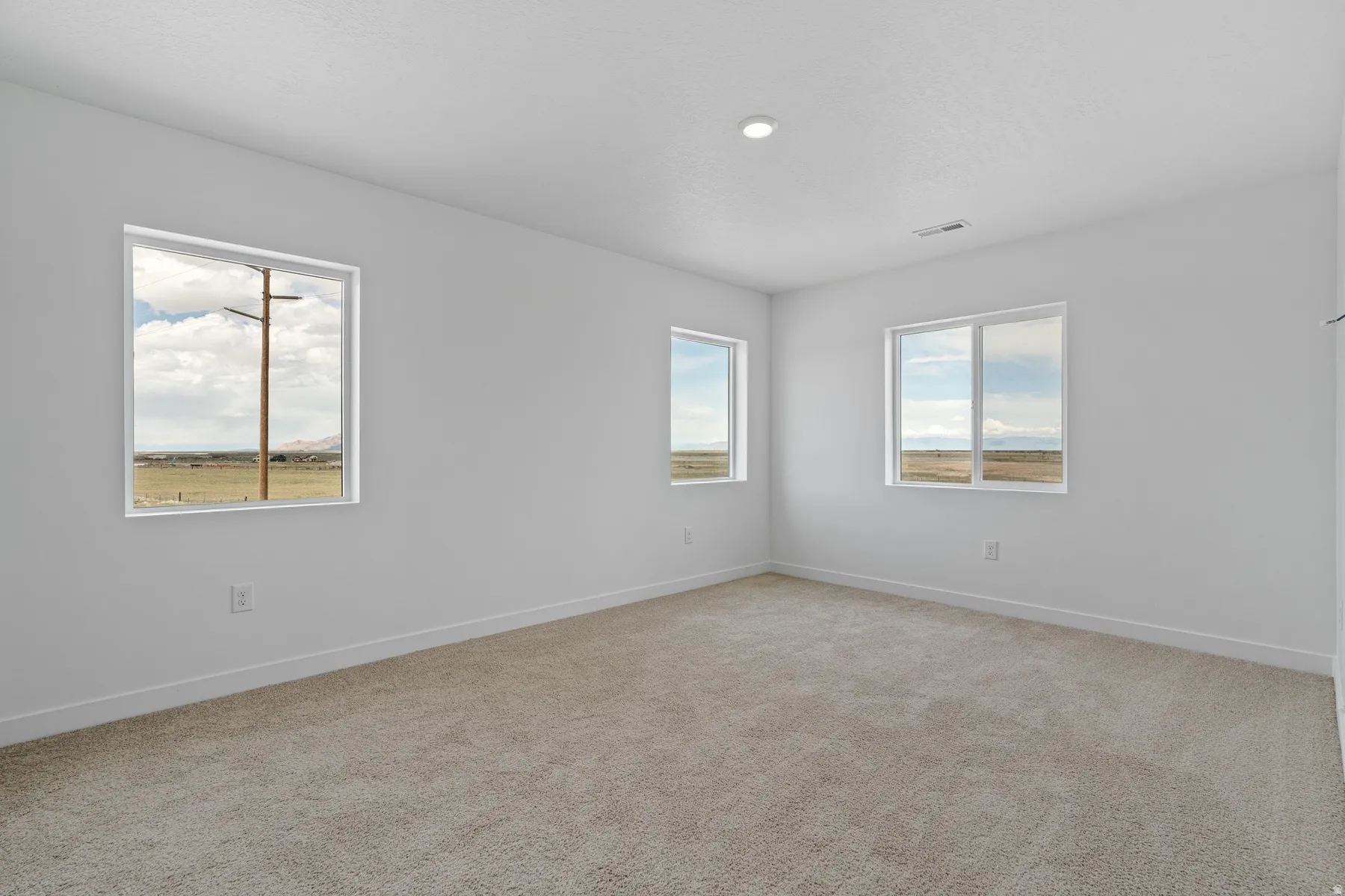 Spacious room featuring neutral carpeting, multiple windows providing natural light, a recessed ceiling light, white baseboards, and a neutral wall palette