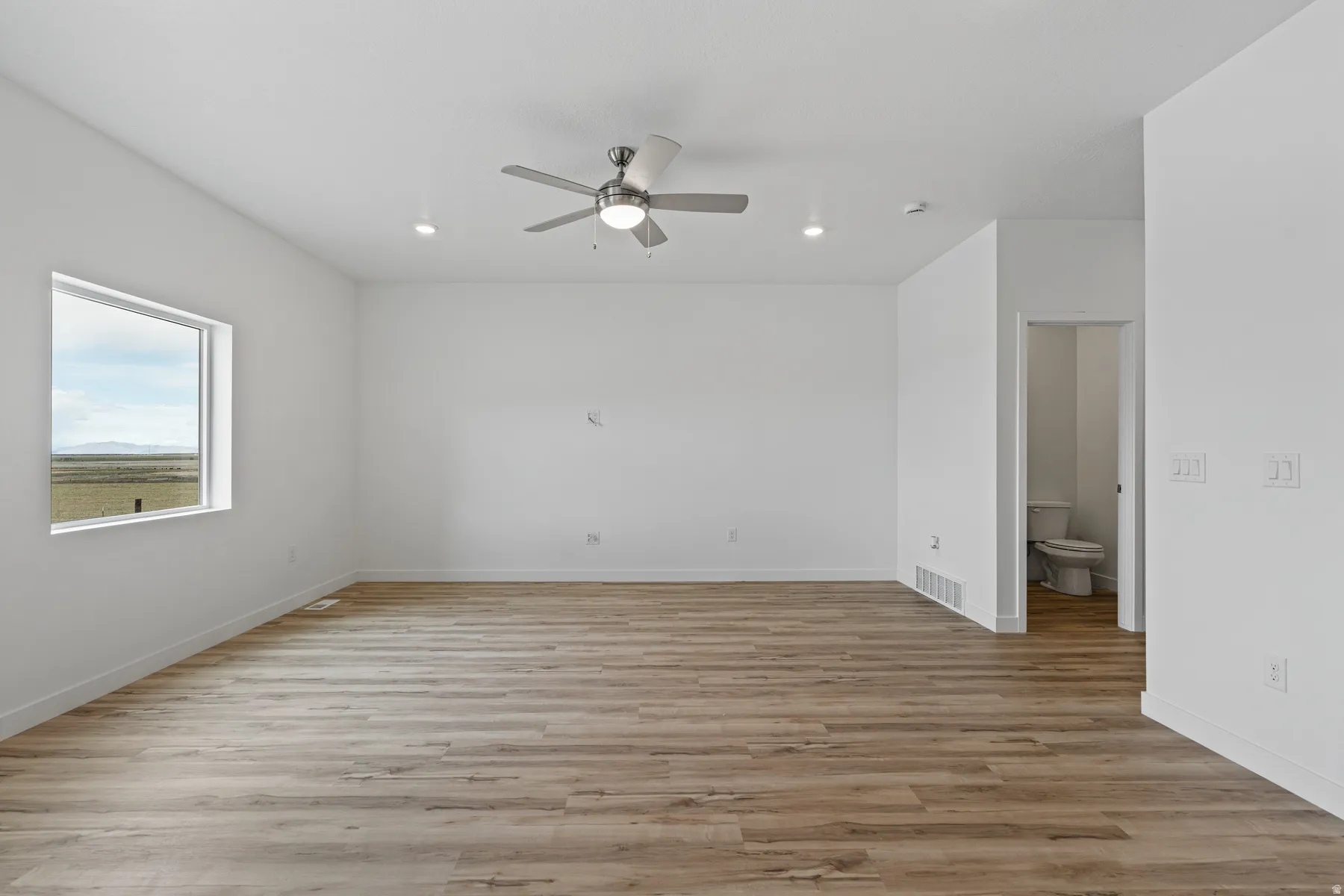 Spacious room featuring wood-finish flooring, recessed lighting, and a ceiling fan with integrated light