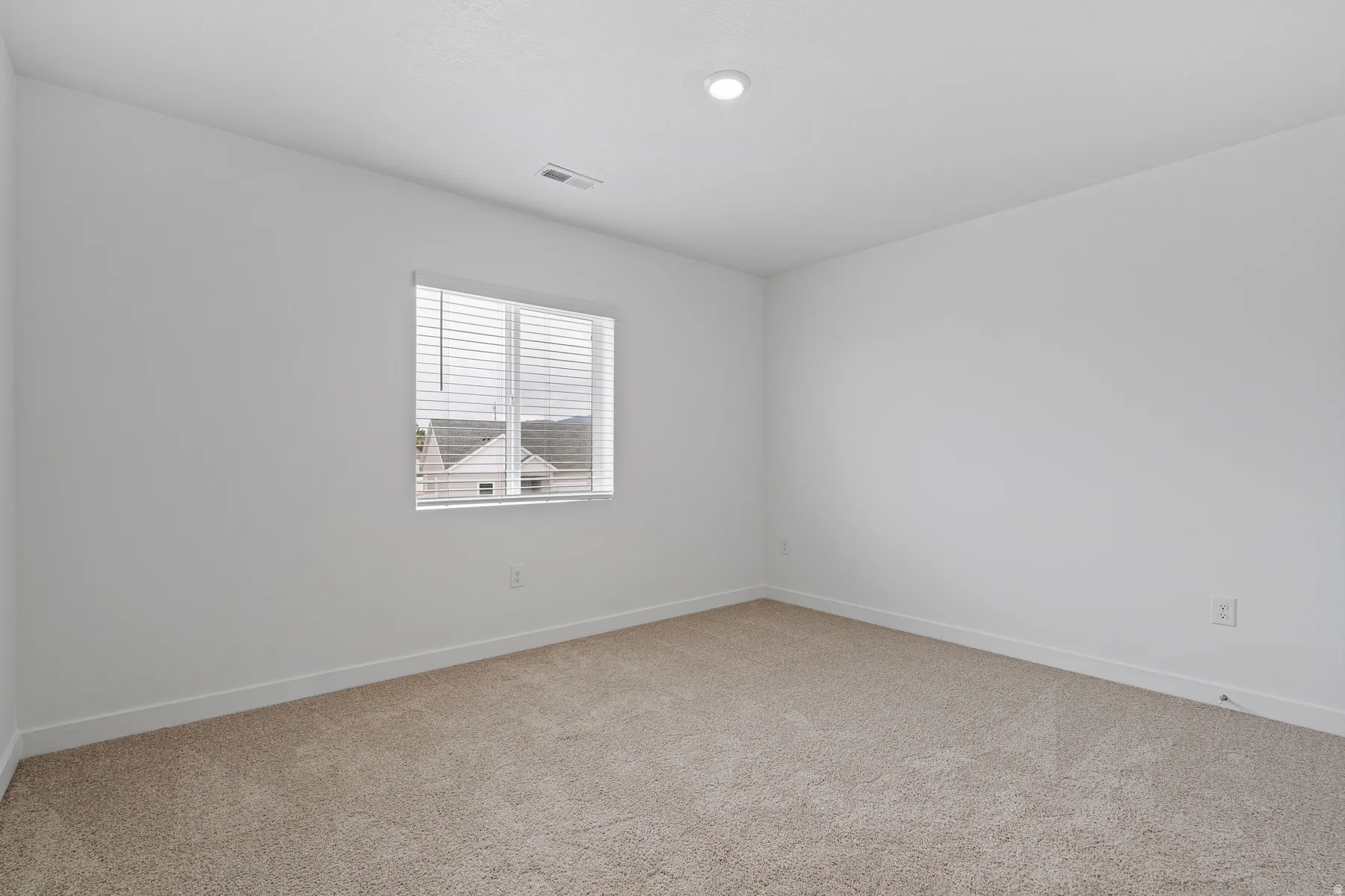 Spacious room featuring neutral carpet flooring, clean white walls, a white baseboard trim, a recessed ceiling light, and a window with horizontal blinds