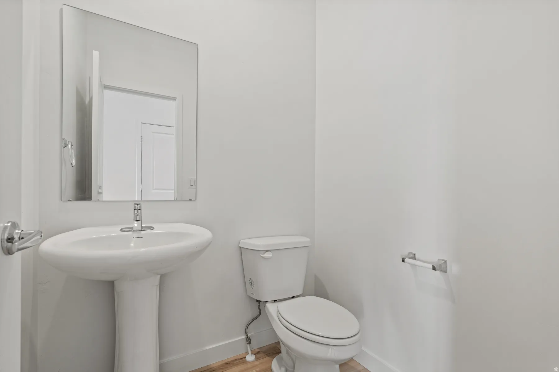 Bathroom featuring a pedestal sink with a chrome faucet, a rectangular wall-mounted mirror, and a white toilet