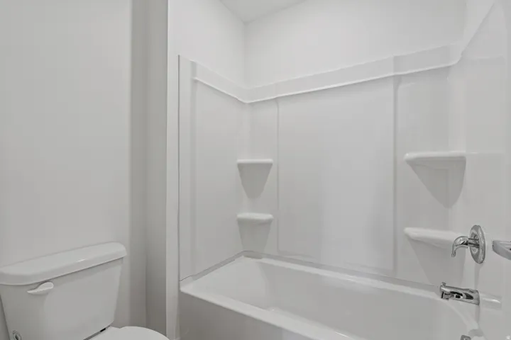 White bathtub and shower combination unit featuring integrated shelving