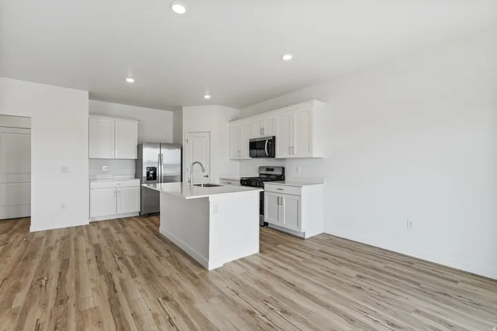 Modern kitchen featuring a central island with an undermount sink, white cabinetry, integrated stainless steel appliances, recessed lighting, and wood-finish flooring