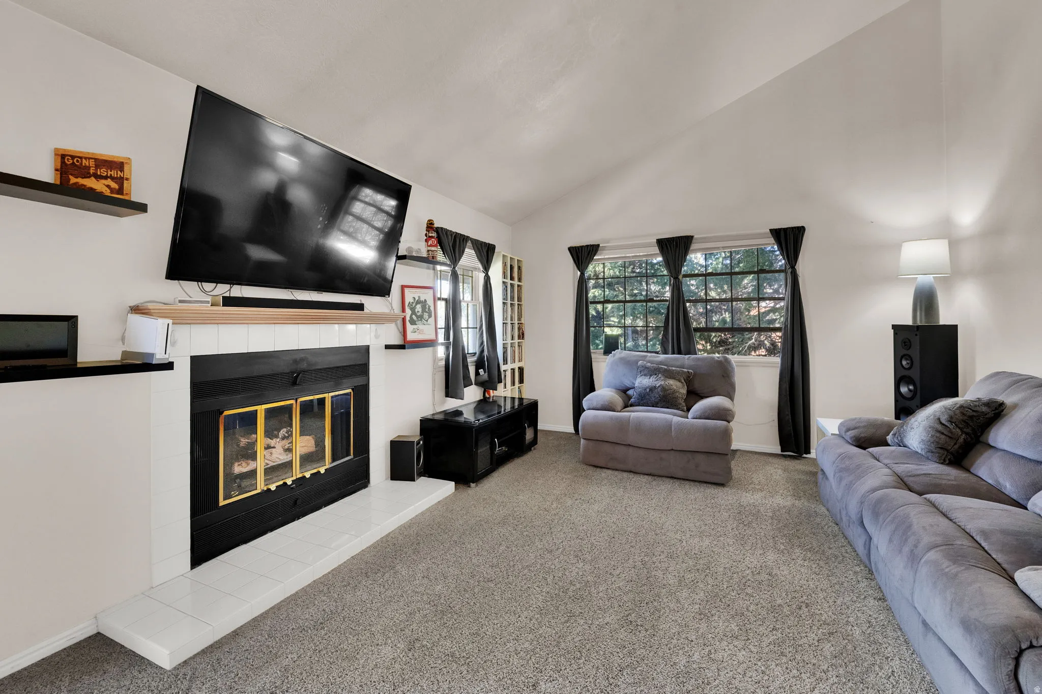 Living room with lofted ceiling, carpet flooring, and a tile fireplace