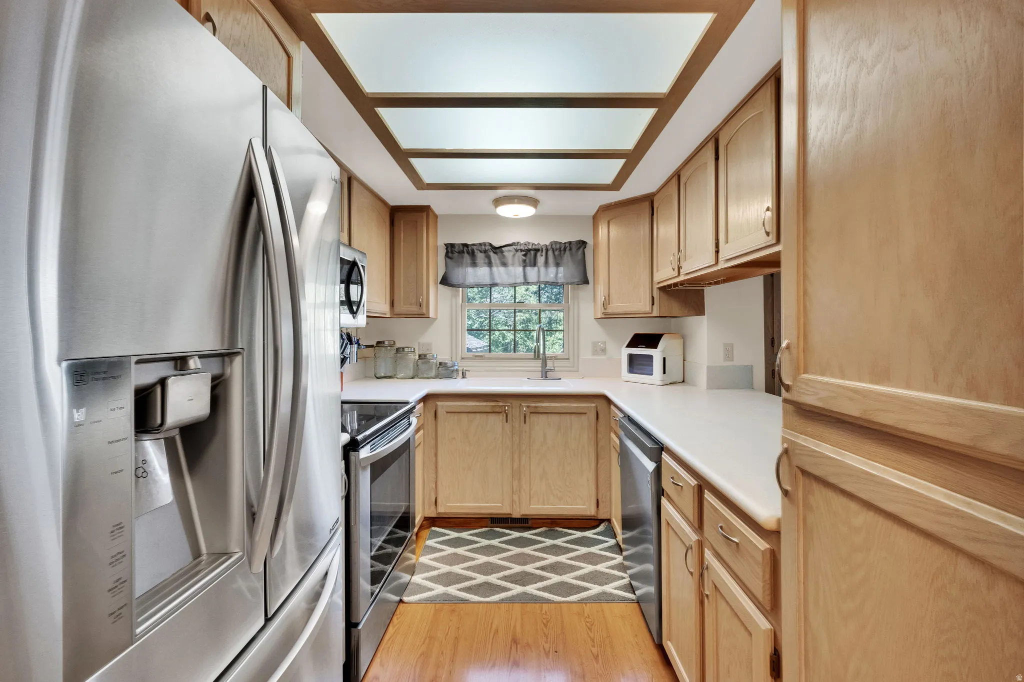 Kitchen with stainless steel appliances, light countertops, light wood finish cabinetry, and light wood-style flooring