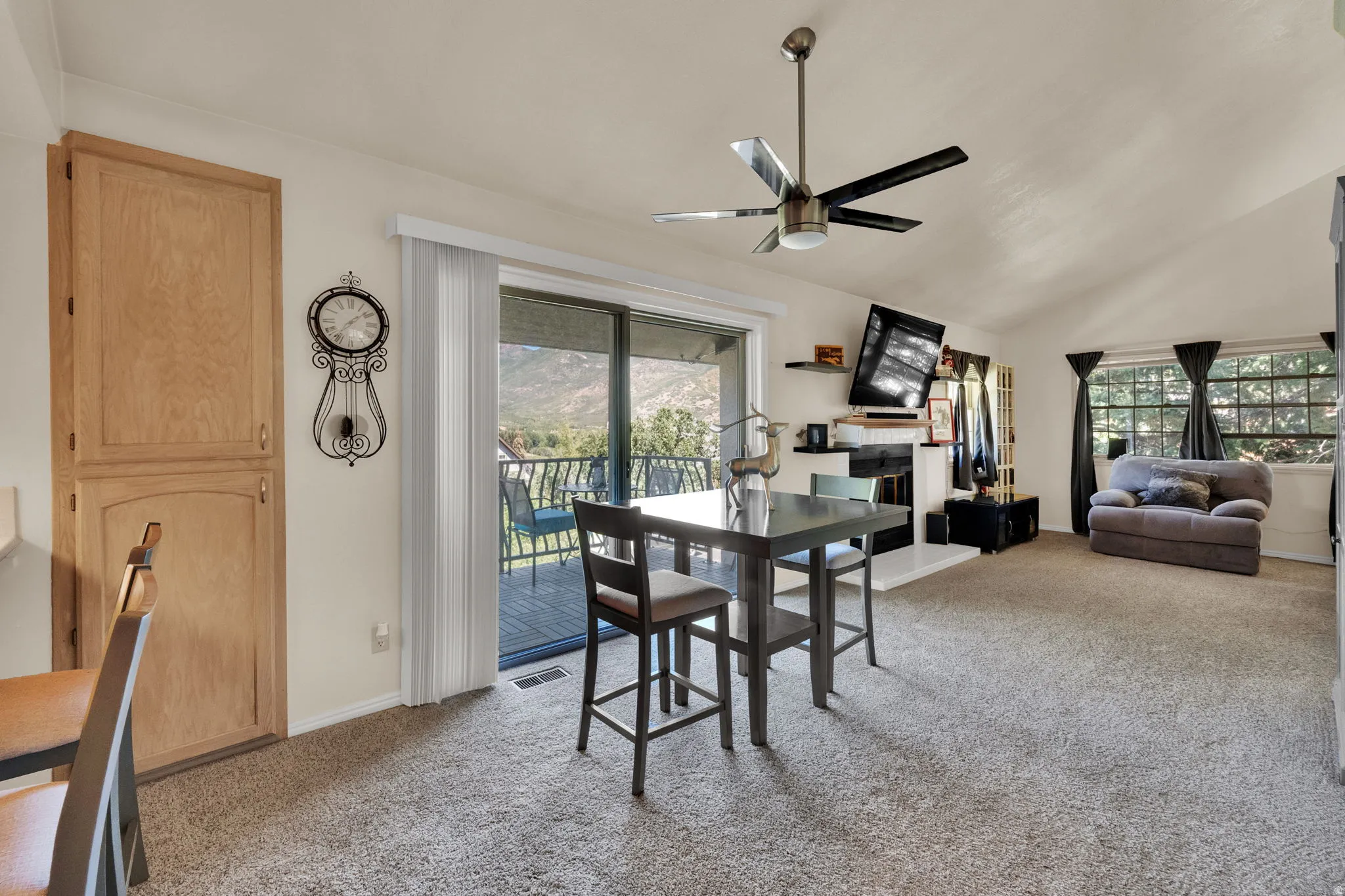 Dining area featuring light colored carpet, a fireplace with raised hearth, ceiling fan, vaulted ceiling, and plenty of natural light