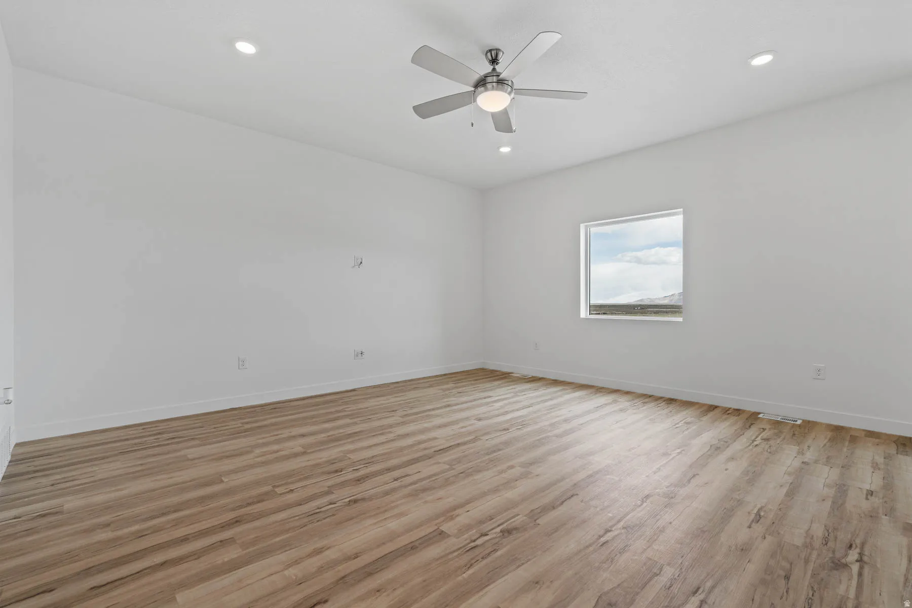 Spacious room featuring wood-finish flooring, recessed lighting, and a ceiling fan with integrated light