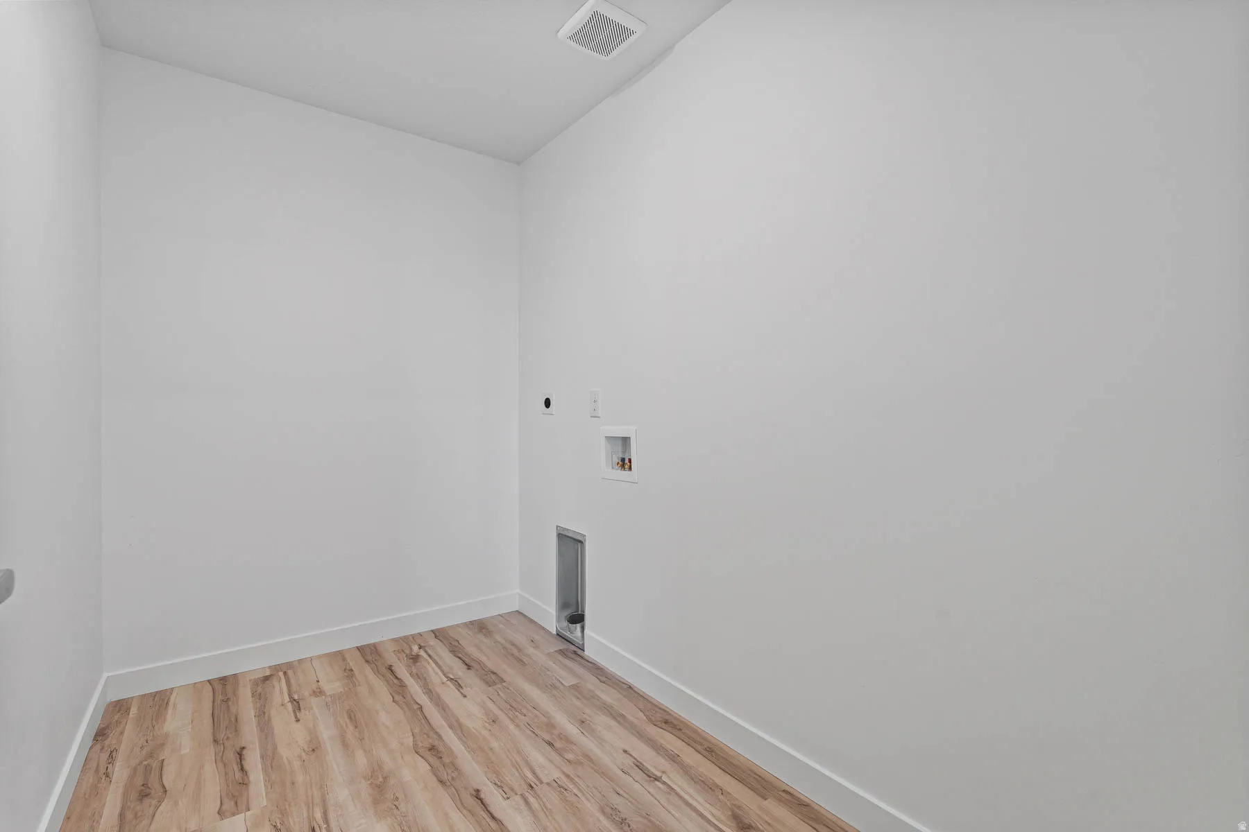 Dedicated laundry space featuring wood-finish flooring, white baseboards, and bright white walls