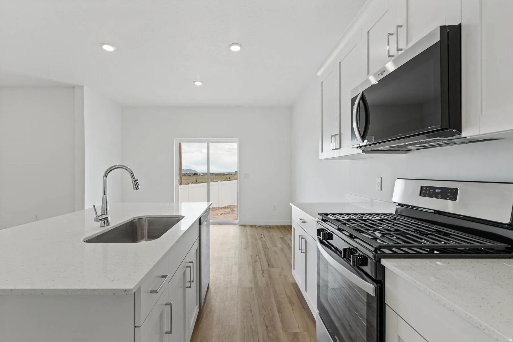 Modern kitchen featuring light cabinetry, stainless steel appliances, quartz countertops, and wood-finish flooring