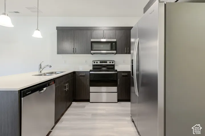 L-shaped kitchen with dark wood-finish cabinetry, stainless steel appliances, light-toned countertops, and light wood-finish flooring
