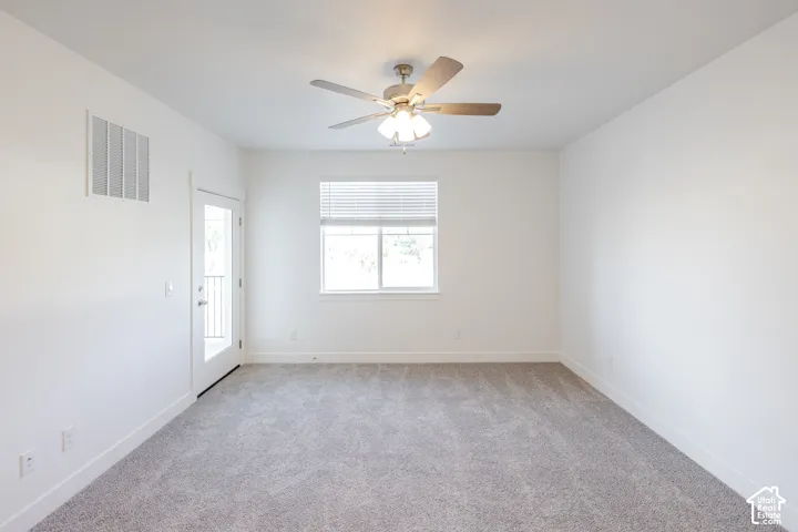 Light-toned carpet flooring, white walls, ceiling fan, and a glass-paneled door leading to an outdoor area