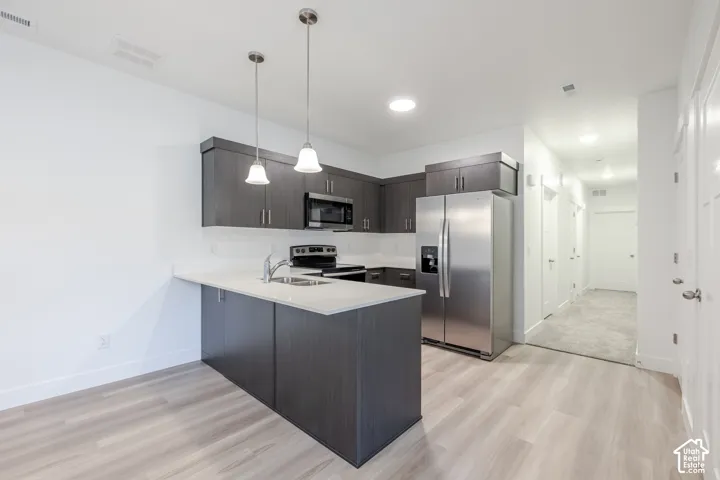 Kitchen featuring wood-finish flooring, dark wood-finish cabinetry, stainless steel appliances, and a light-toned countertop