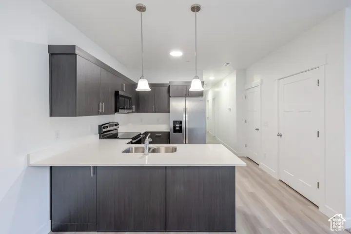 Contemporary kitchen featuring dark wood-finish cabinetry, stainless steel appliances, a double basin sink, and pendant lighting