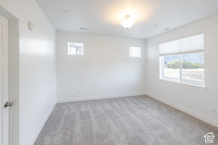 Neutral tone wall paint, contemporary ceiling light fixture, grey patterned carpeting, and multiple windows with blinds