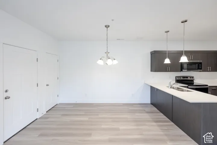 Wood-finish flooring, white walls, and a modern kitchen featuring dark wood cabinetry, white countertops, and stainless steel appliances