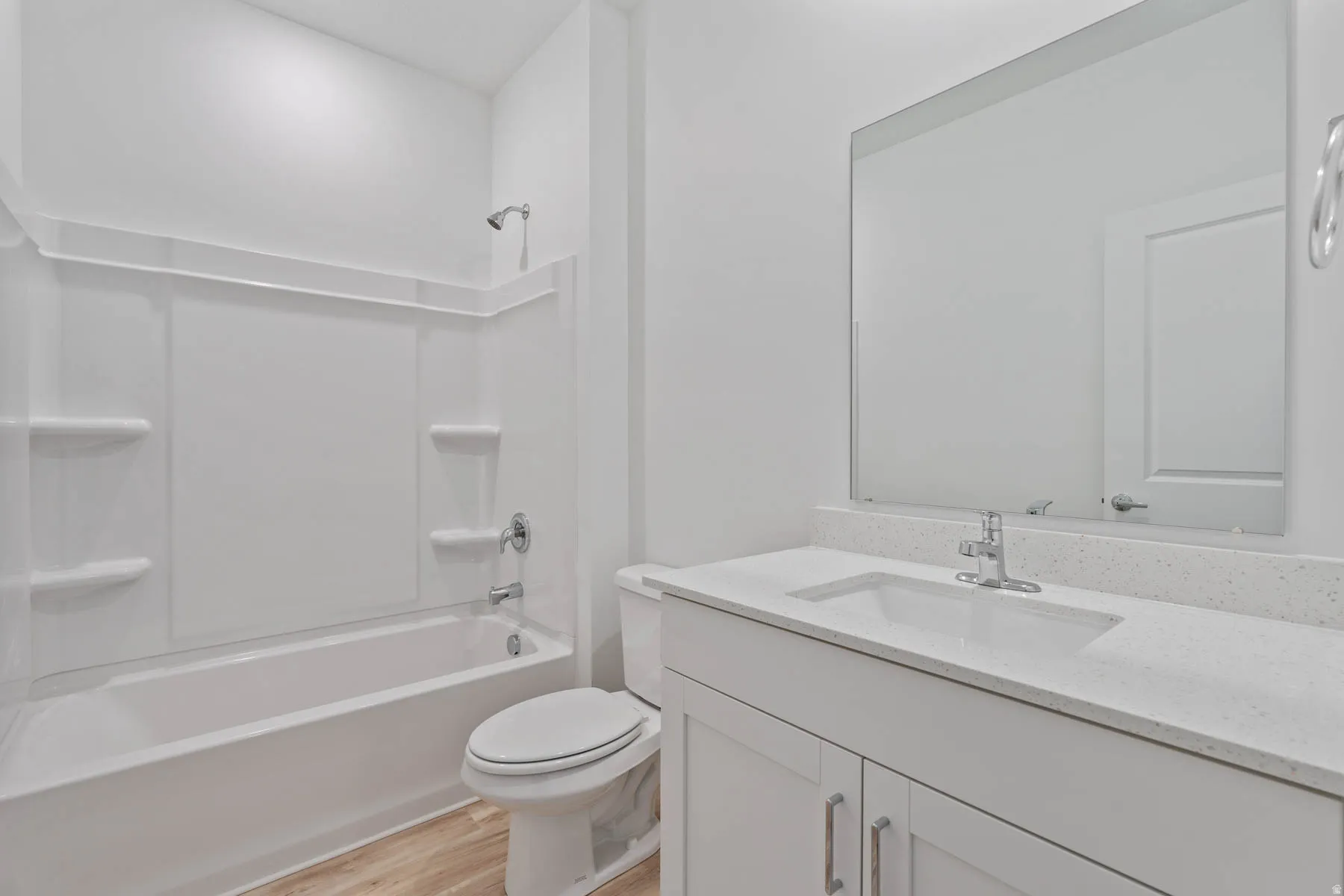 Bathroom featuring a white bathtub and shower surround, a single vanity with a white countertop and integrated sink, a large frameless mirror, and wood-finish flooring