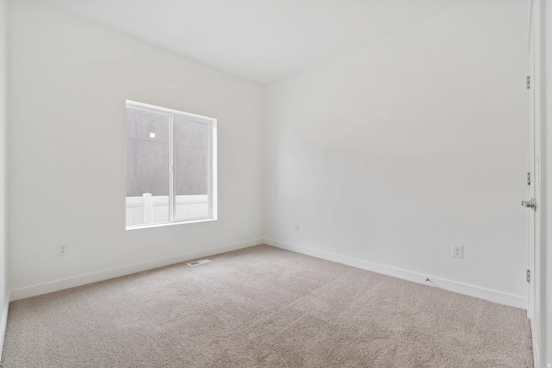 Neutral-toned carpet flooring, white painted walls, white trim, a single window with white framing, and a white door with a silver handle