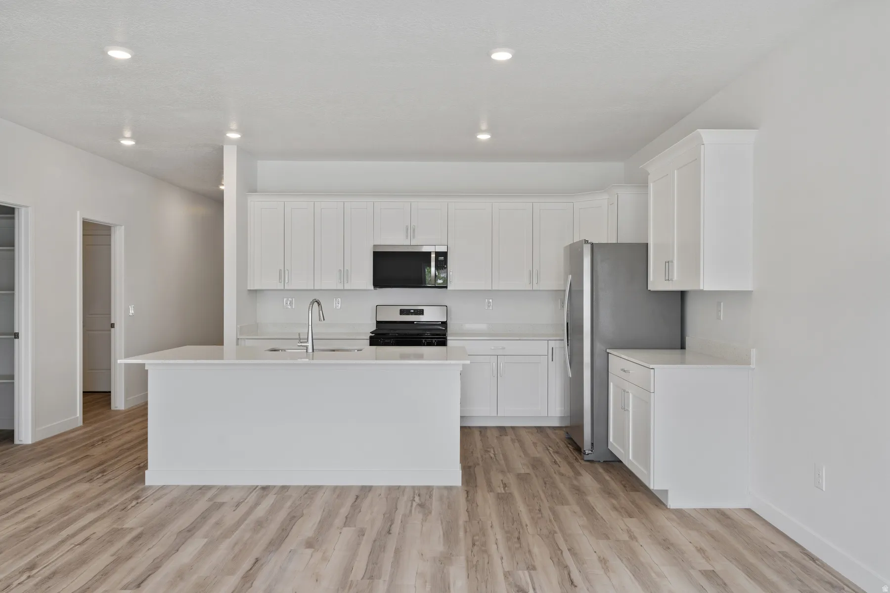 Contemporary kitchen featuring a large island, white cabinetry, stainless steel appliances, and wood-finish flooring