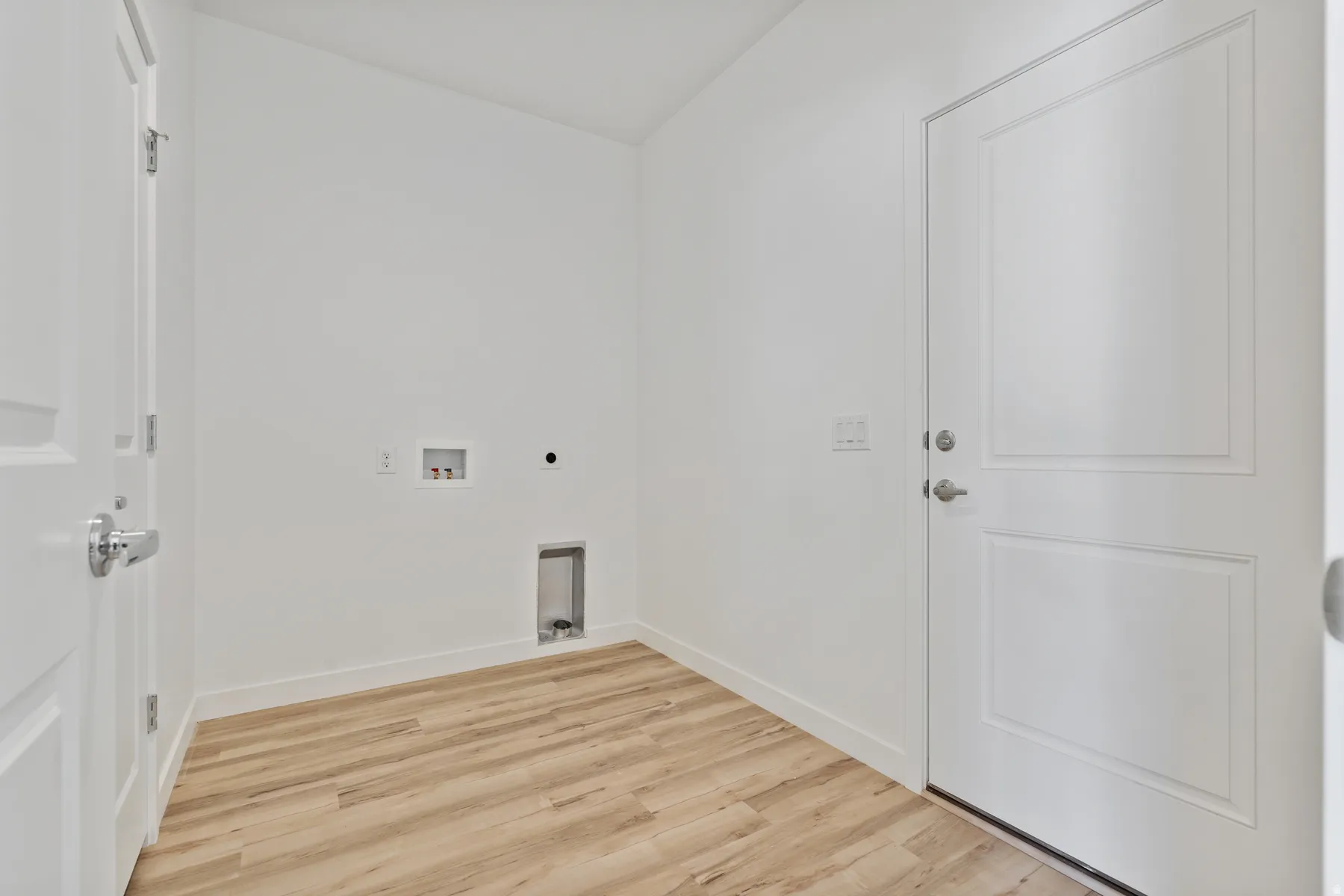 Dedicated utility space featuring light wood-finish flooring, white baseboards, and bright white walls