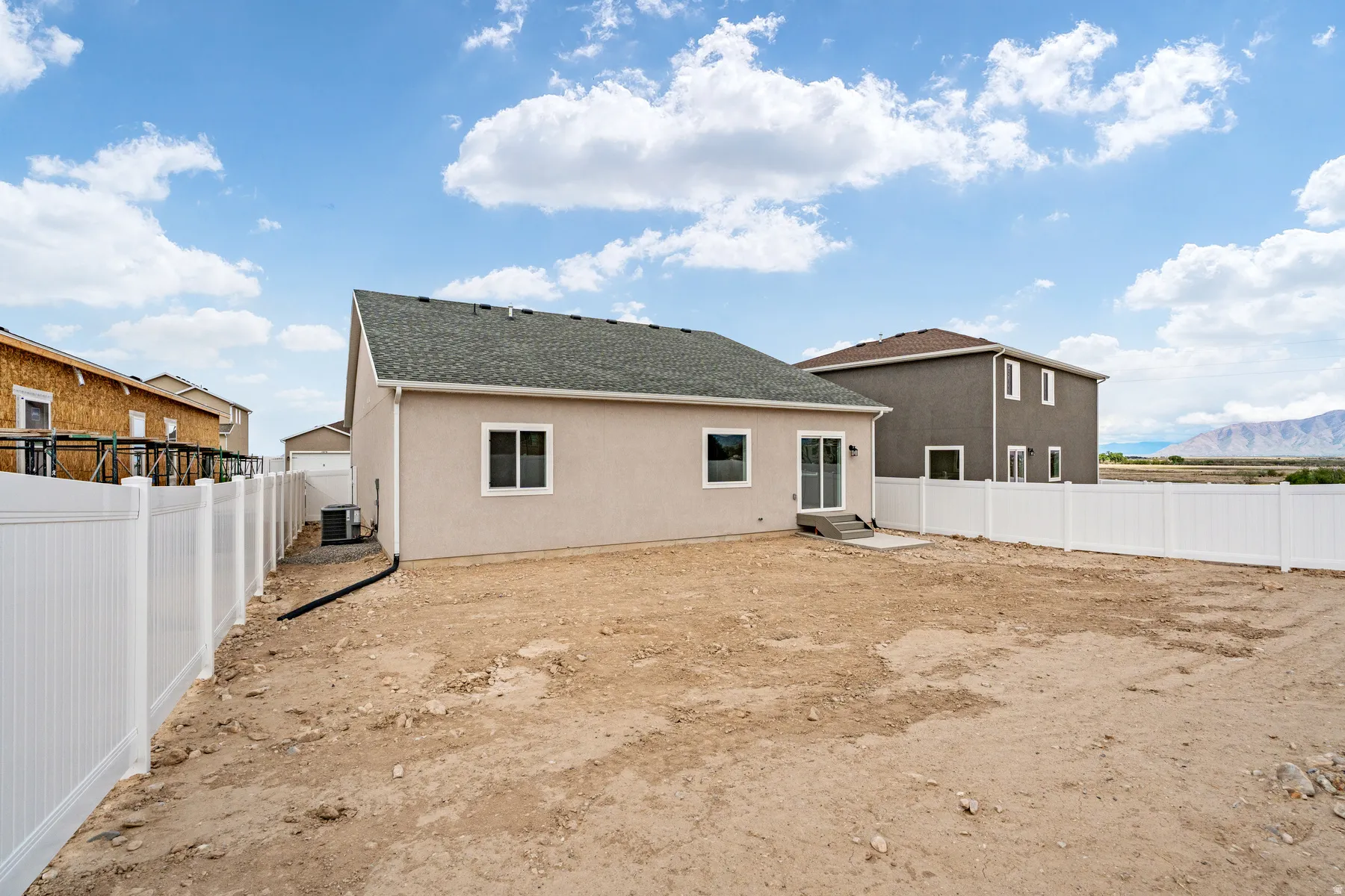 Rear exterior featuring a stucco facade, dark shingle roof, and white vinyl perimeter fencing