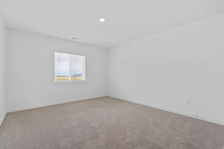 Neutral-toned carpeting paired with white walls, a single window with horizontal blinds, and a ceiling-mounted recessed light