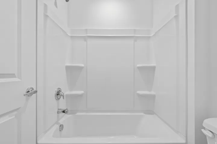 White alcove bathtub and shower combination featuring integrated shelving