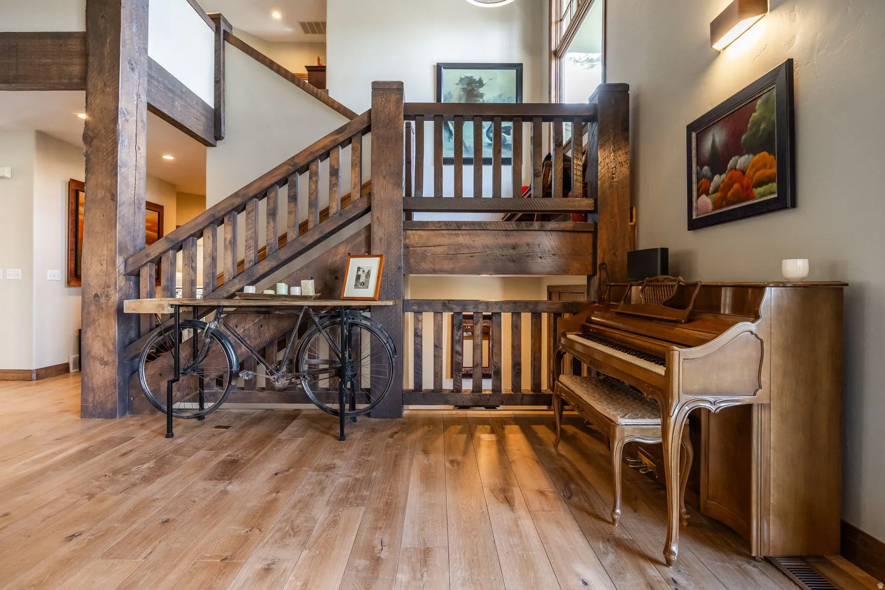 Grand entryway featuring broad plank wood-finish flooring, a substantial wood staircase with balusters, exposed structural wood beams, and neutral wall paint