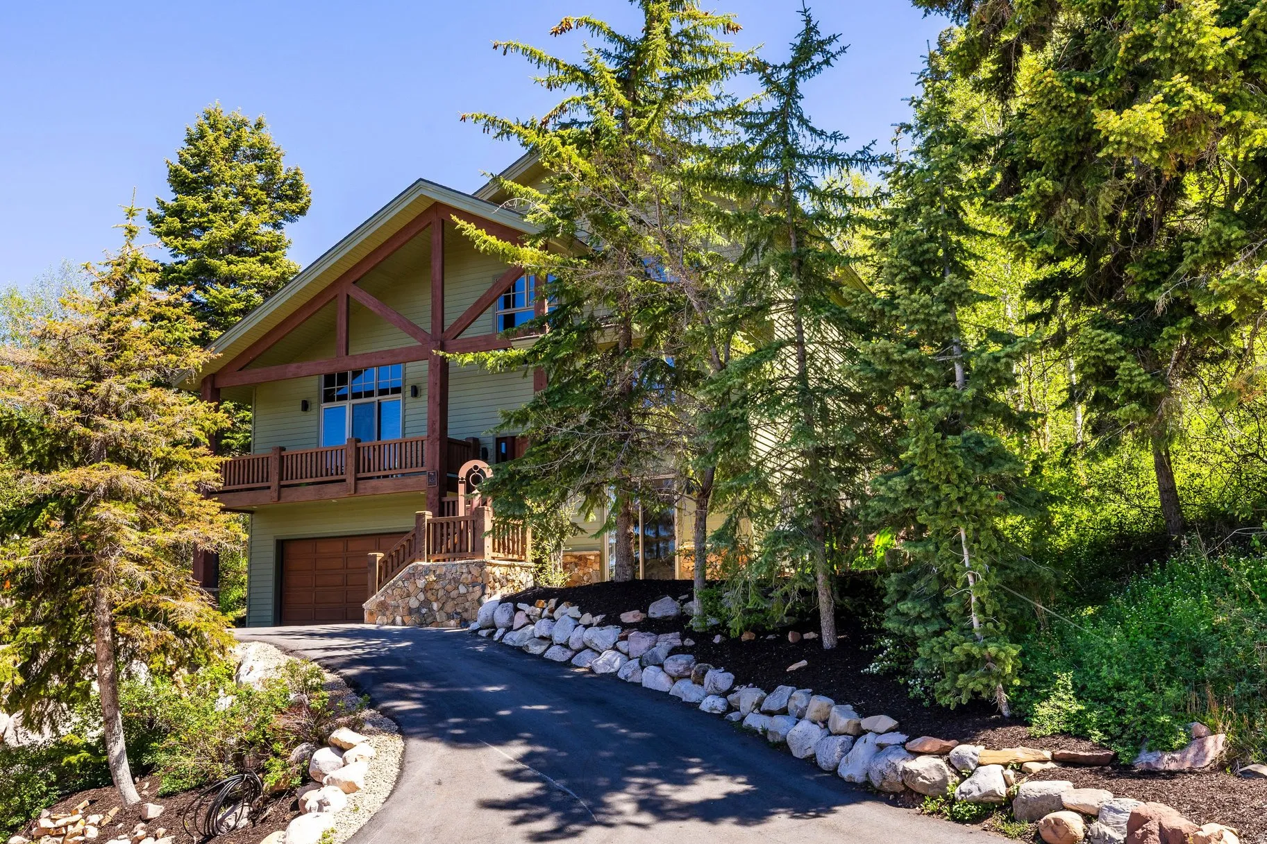 Exterior featuring a wood-siding facade, exposed timber framing, an attached balcony, a wood-finish garage door, and a stone foundation
