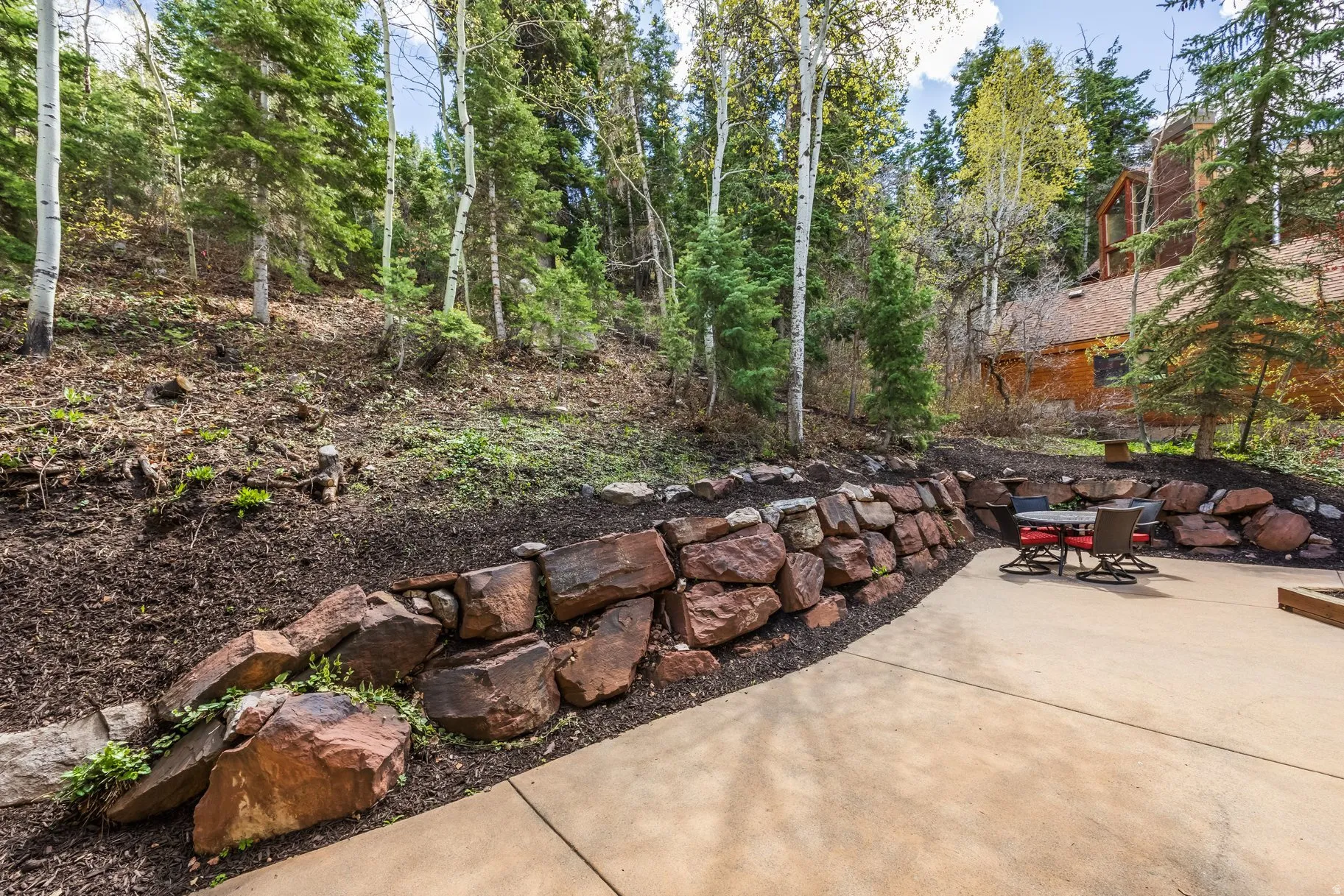 Concrete patio area bordered by a natural stone retaining wall and mature trees