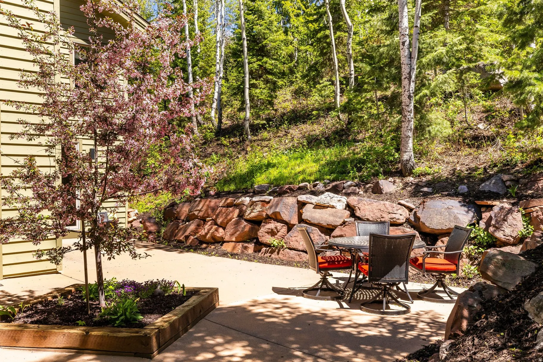 Patio space featuring a stone retaining wall, mature trees, and a tree with red foliage