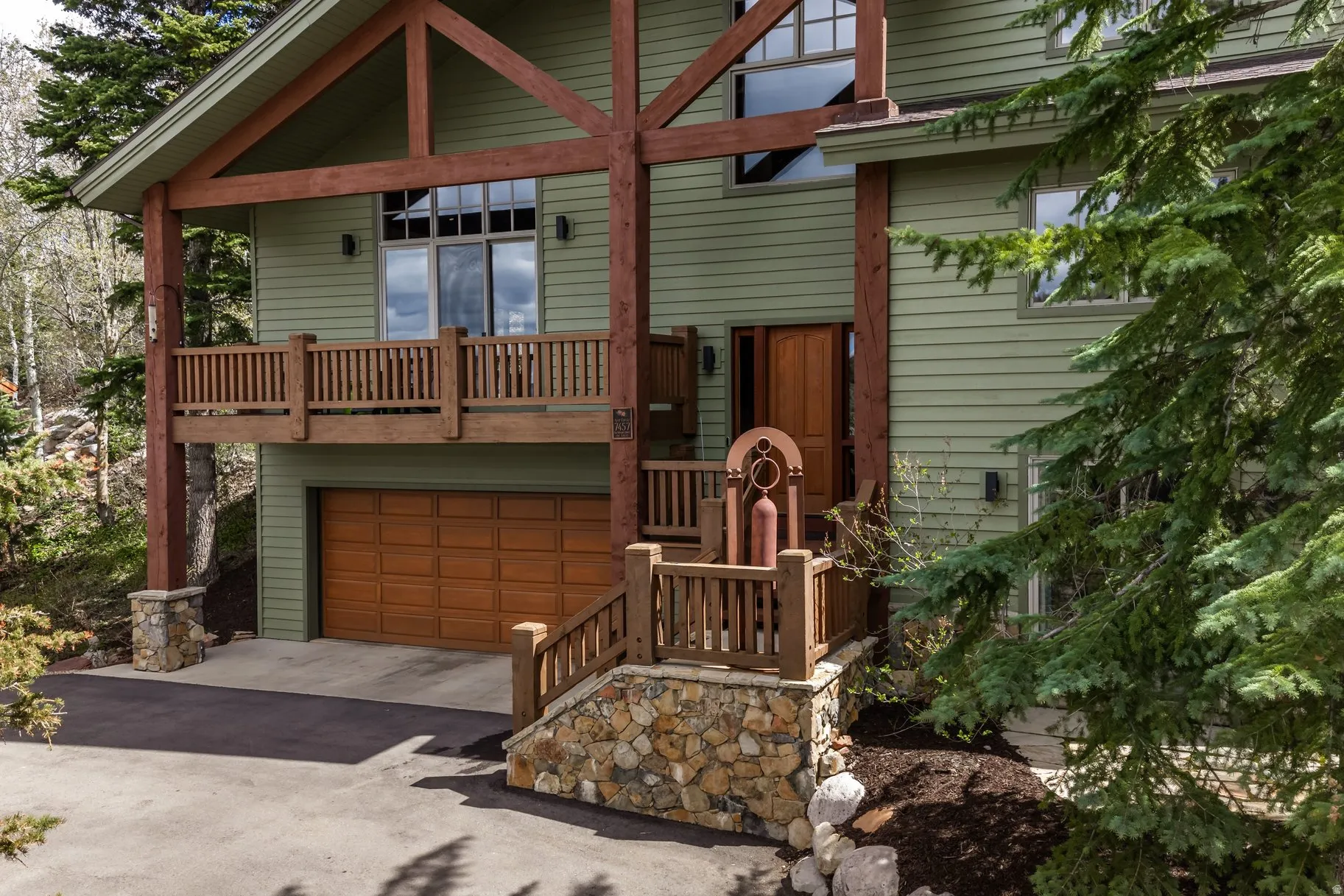 Crafted exterior featuring green siding, exposed wood beams, and a natural wood garage door