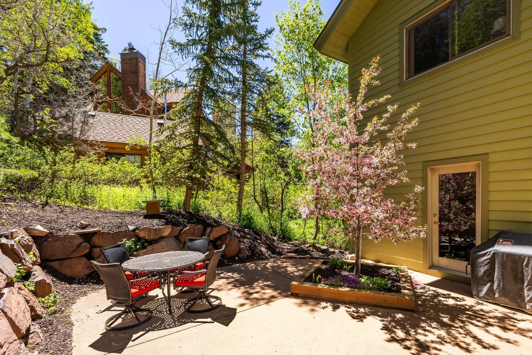 Exterior patio featuring a concrete surface, a stone retaining wall, and a raised planter with a flowering tree