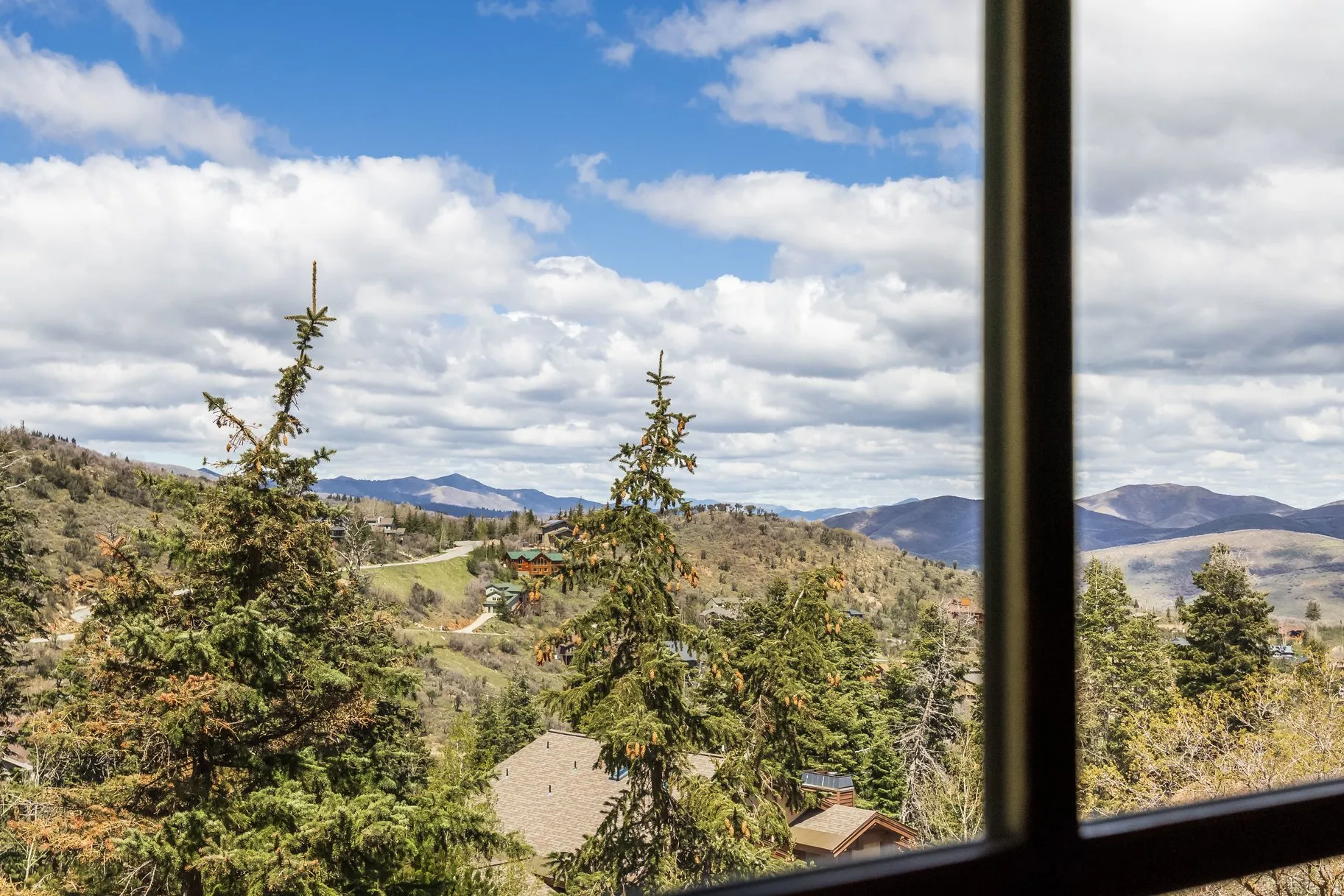 Framed mountain terrain with distant peaks, featuring evergreen trees and scattered rooftops