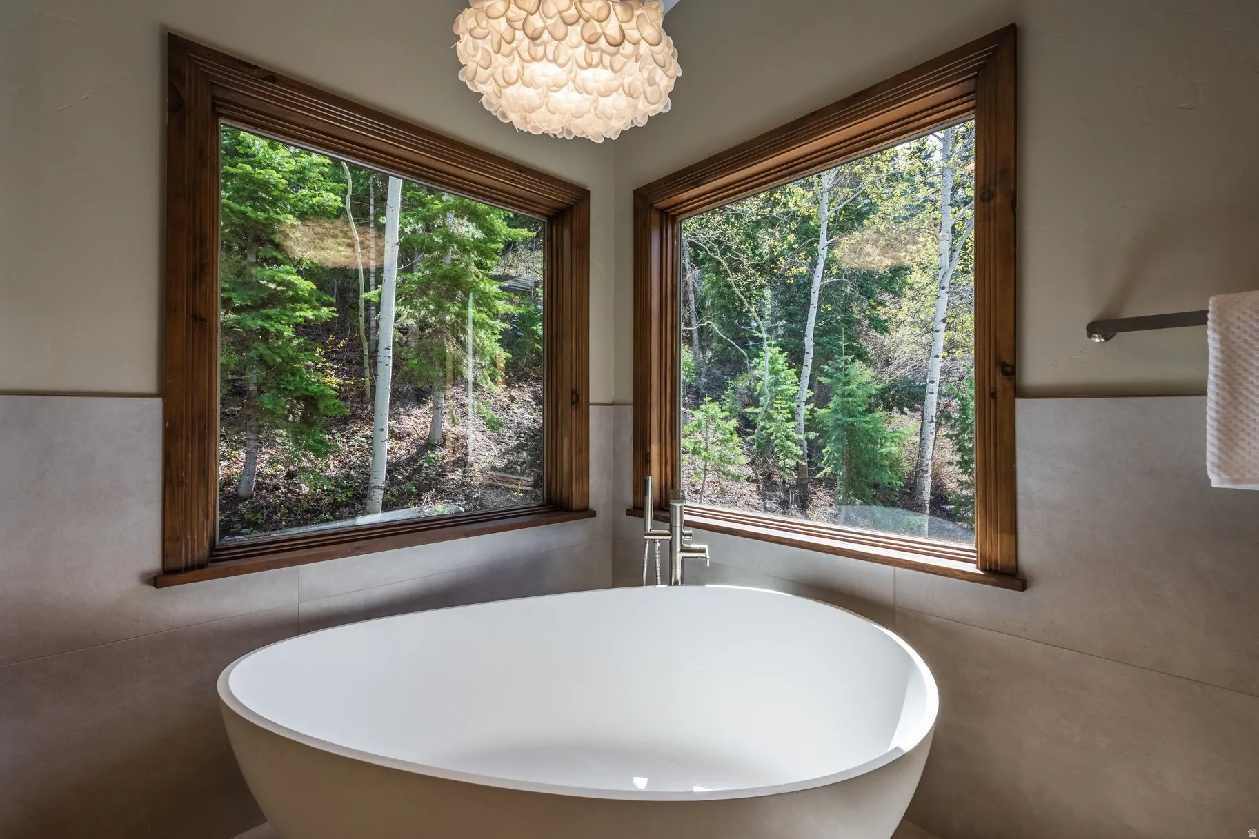 Freestanding soaking tub with brushed nickel floor-mounted faucet, complemented by two large picture windows with natural wood trim