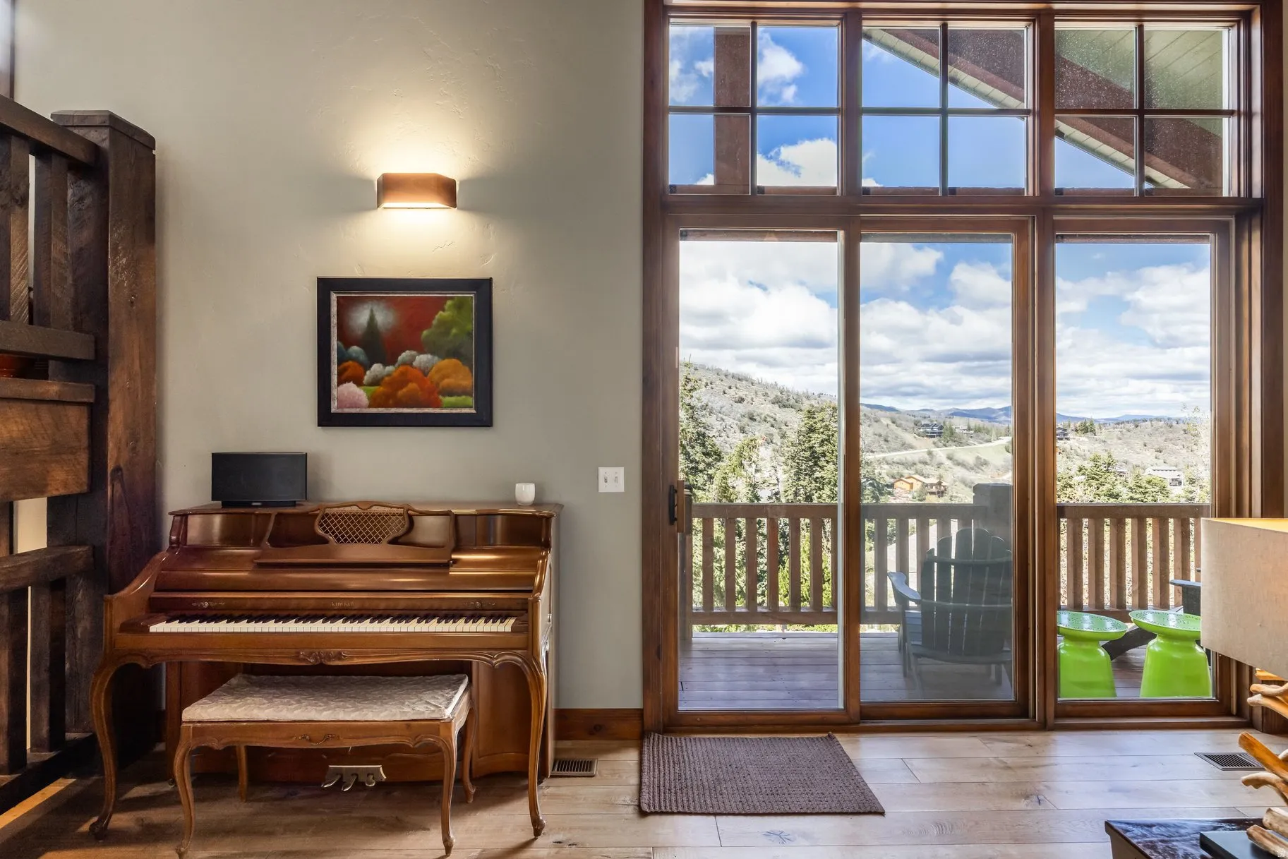 Expansive wood-framed windows and a sliding glass door reveal a private balcony with a wooden railing and a mountain backdrop