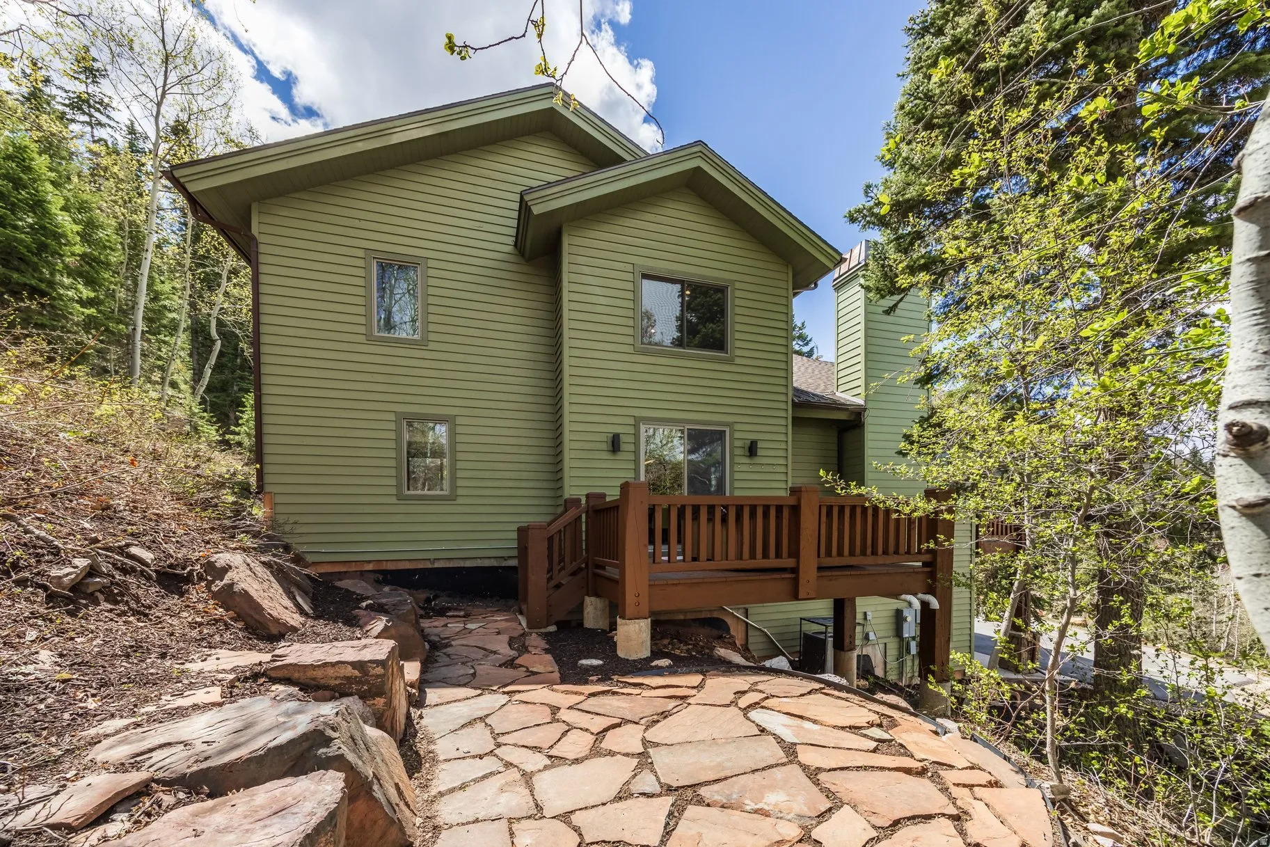 Exterior featuring horizontal siding in an earthy tone, a wood-finish deck with railings, and a stone-paved patio