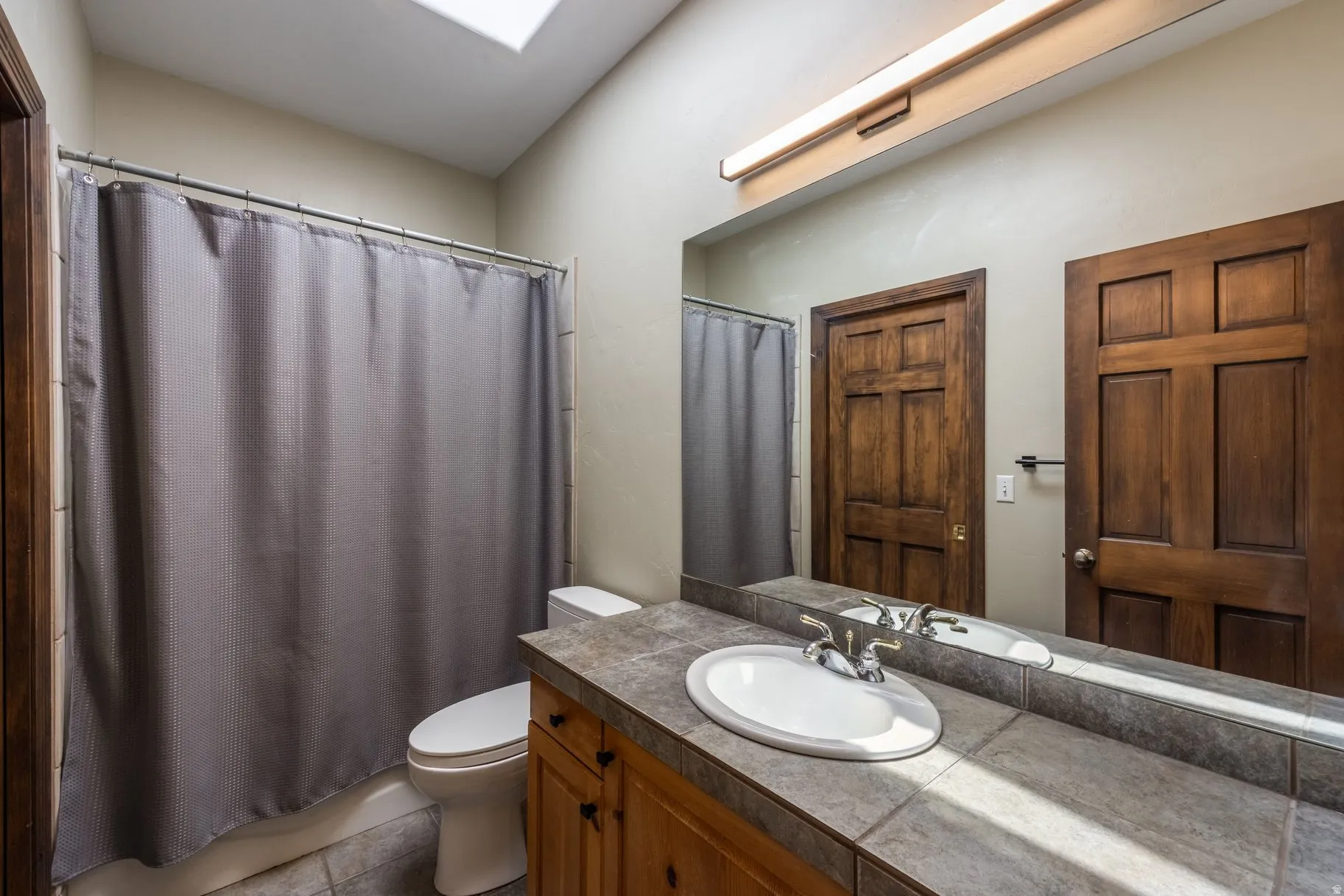 Bathroom featuring a skylight, tile flooring, wood-finish vanity with an oval sink, and a tiled countertop