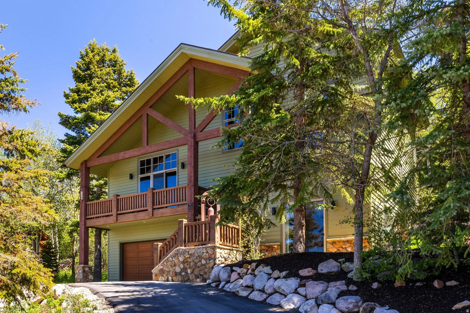Spacious multi-level home featuring a light green exterior, a prominent wooden beam balcony, and a stone-clad foundation