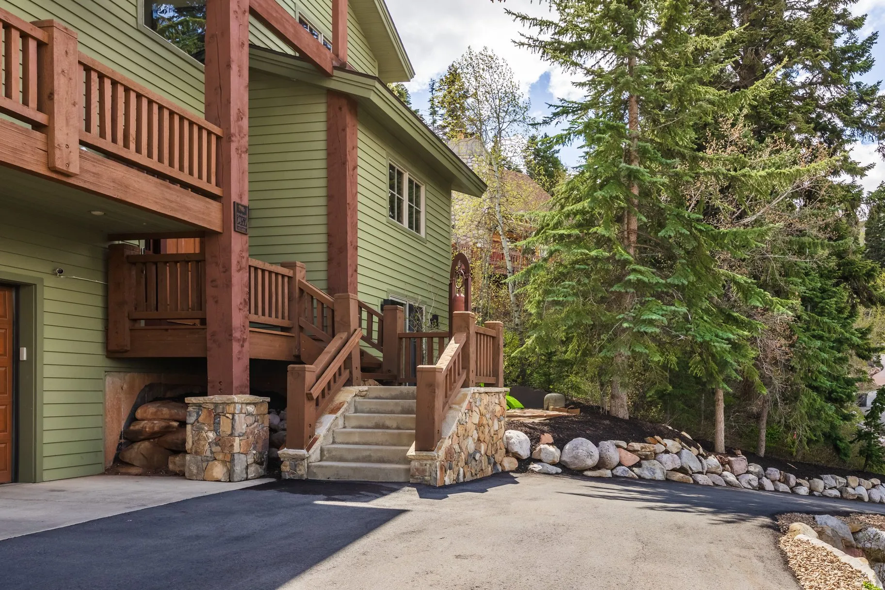 Multi-level exterior featuring a light green siding facade, wood-finish balconies, and stone masonry accents