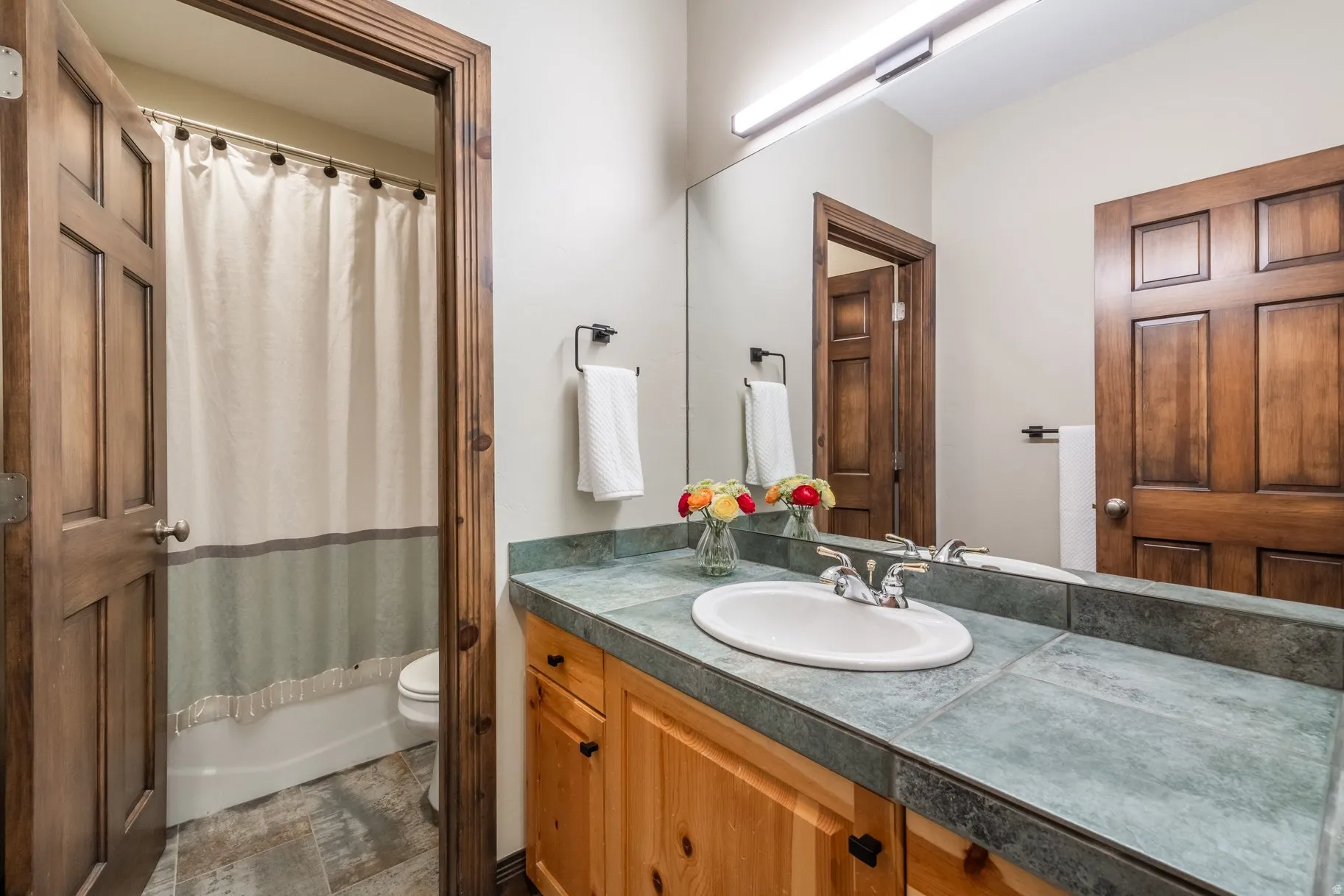 Bathroom featuring a wood-finish vanity with panel doors and matte black hardware, slate tile countertop, and an undermount sink with a chrome faucet